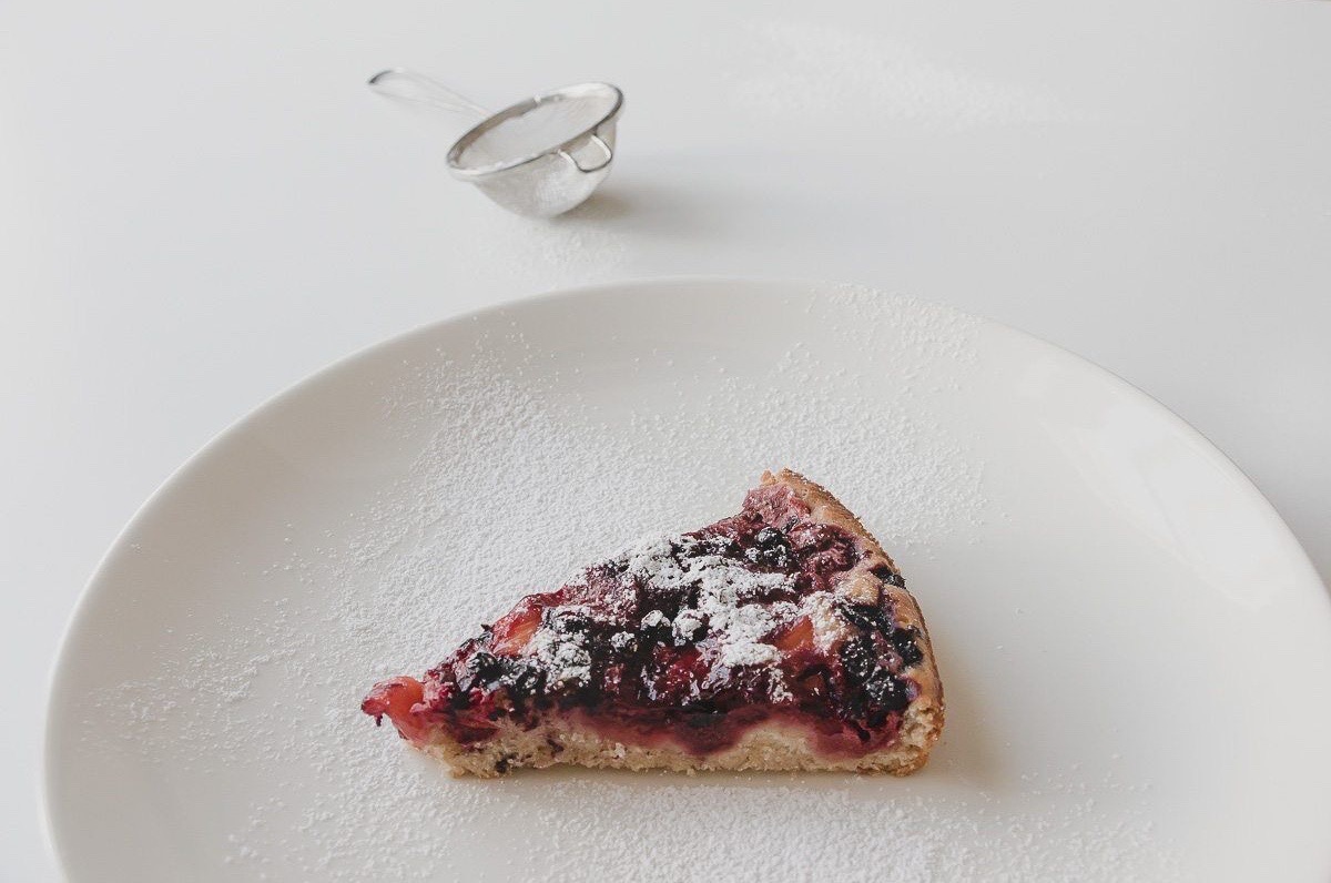 vegan pineapple berry pie slice, dusted with powdered sugar on a white plate