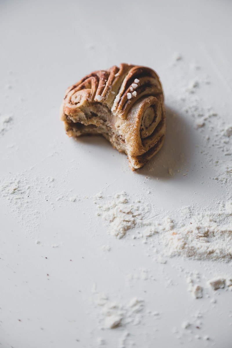 a half eaten vegan cinnamon bun and flour on a white table