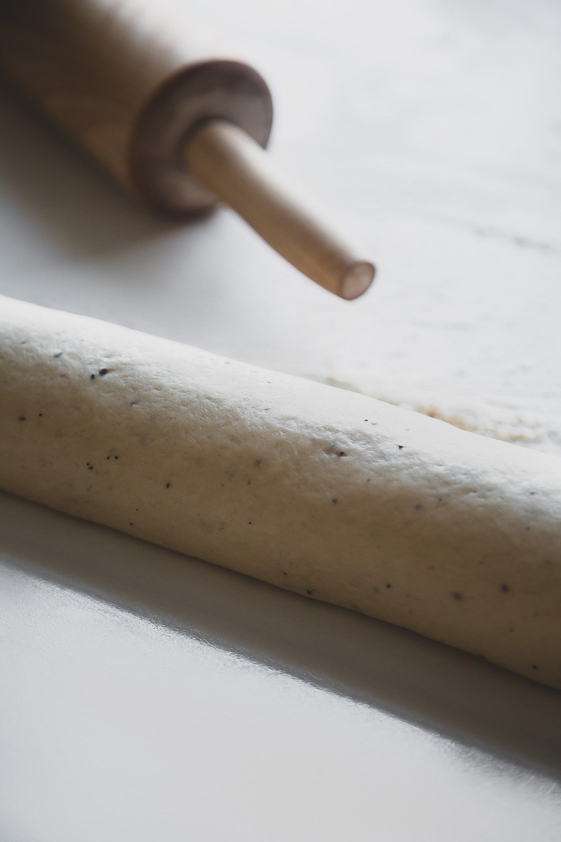 a traditional wooden rolling pin and ready to be cut dough roll of cinnamon buns