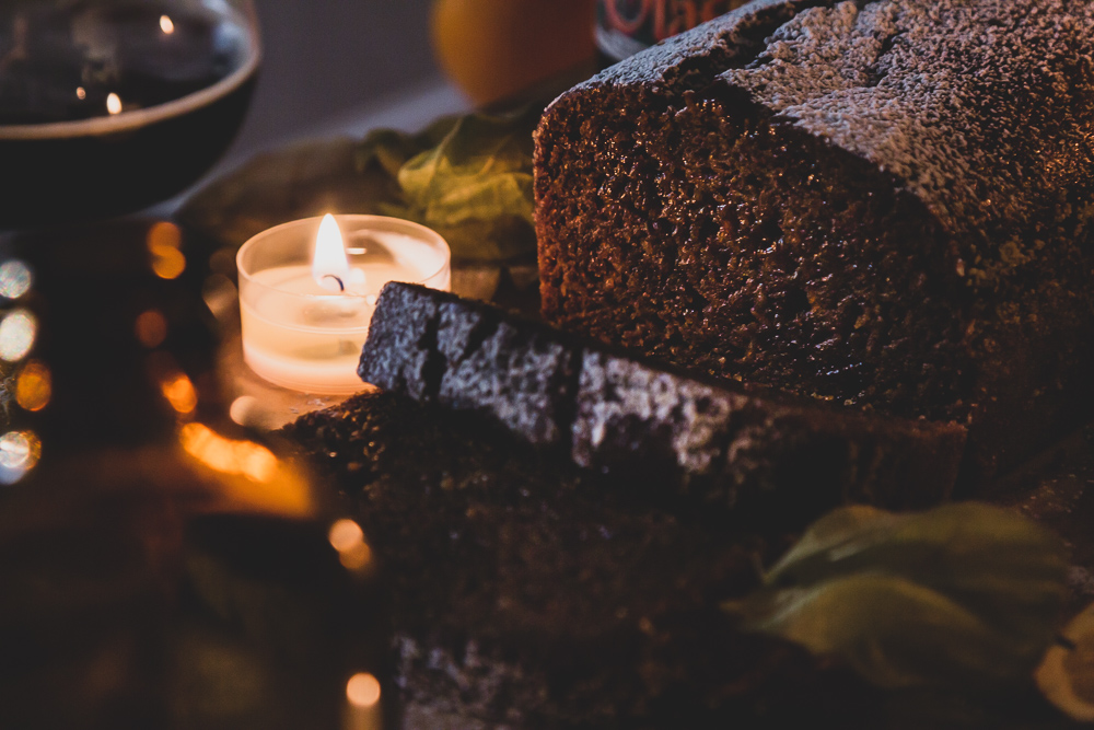 Vegan Christmas Loaf Cake sliced on a decorated cutting board with candles and a glass of dark beer