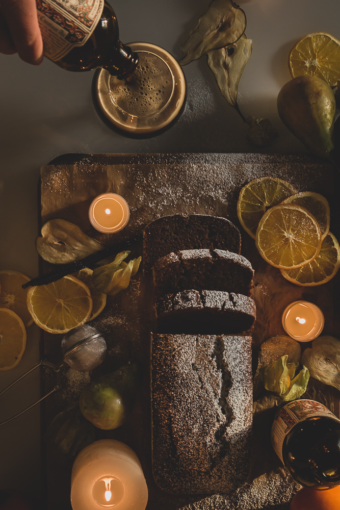 Decadent vegan Christmas Loaf Cake, fruit and some candles on a table. A man is pouring Ale into a glass.