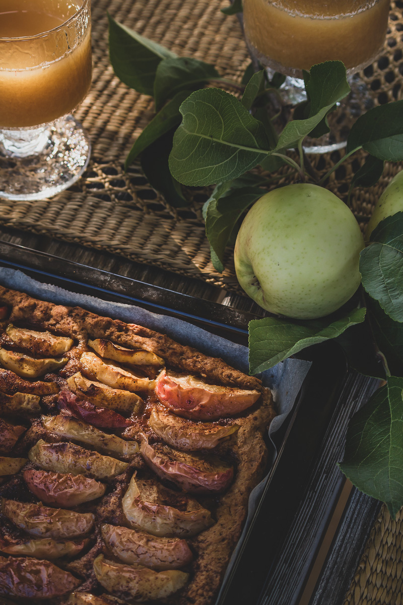 Freshly baked apple pie, two glasses of apple juice and fresh apple brach on a table.