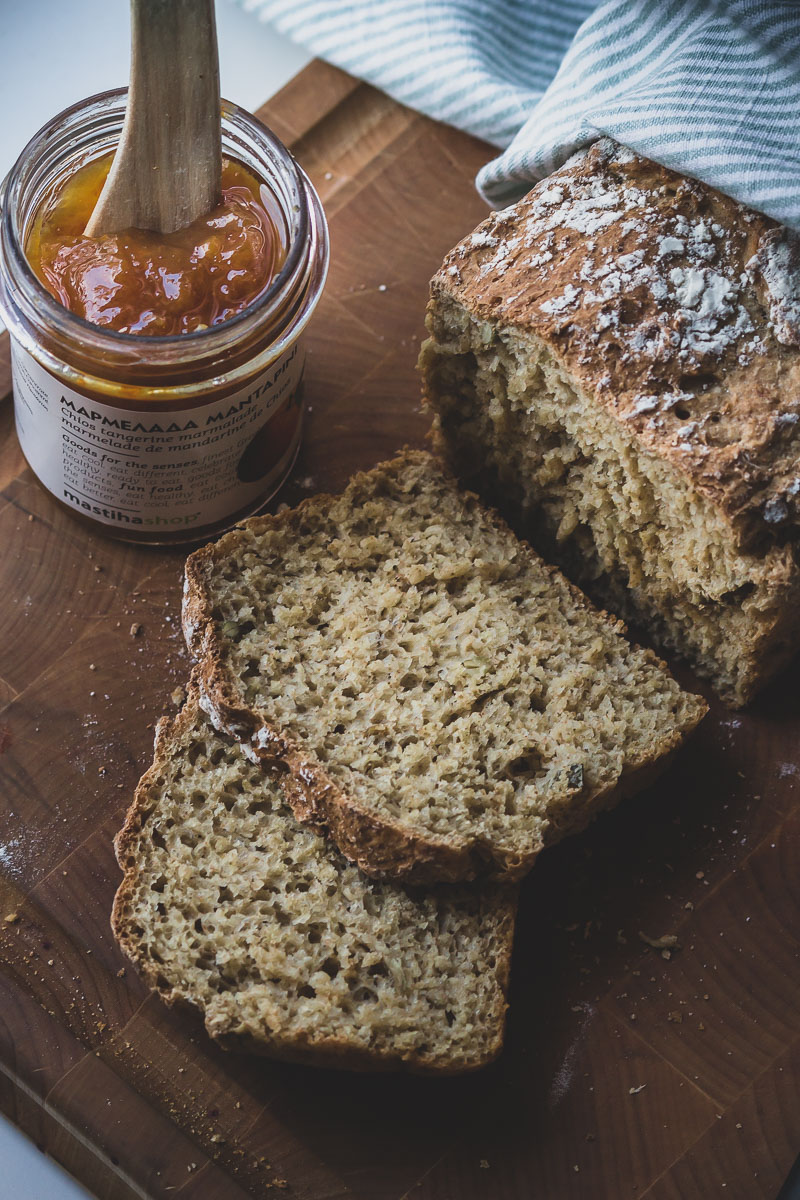 Sliced no-knead breakfast bread on a wooden cutting board next to a jar or mandarin marmalade.
