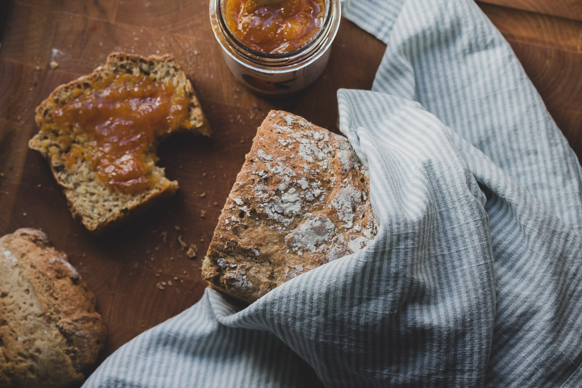 Breakfast bread loaf and a slice that is topped with mandarin marmalade on a wooden cutting board.