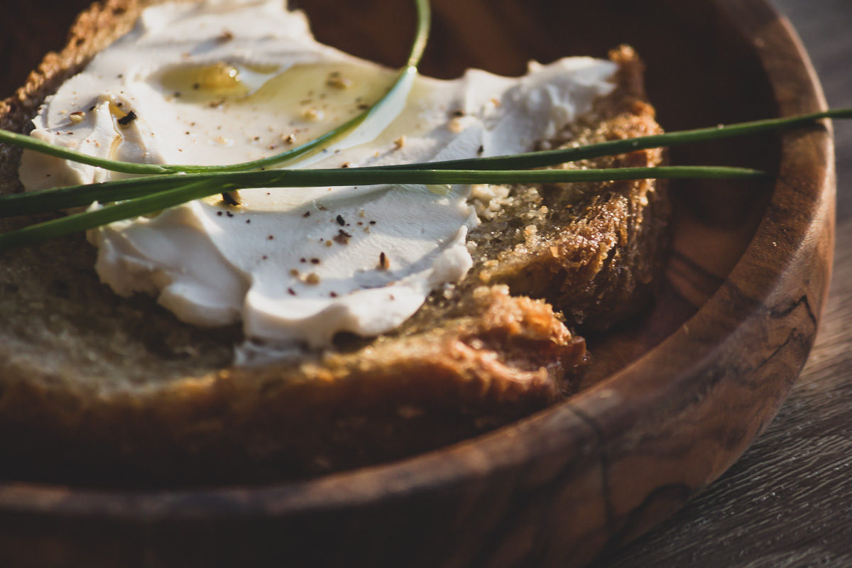 A close up of a crunchy slice of garlic bread topped with vegan cream cheese, chives and olive oil.