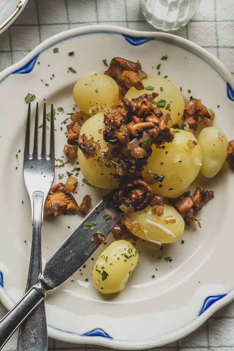 A close up of a plate of chanterelles and boiled summer potatoes decorated with dried lovage.