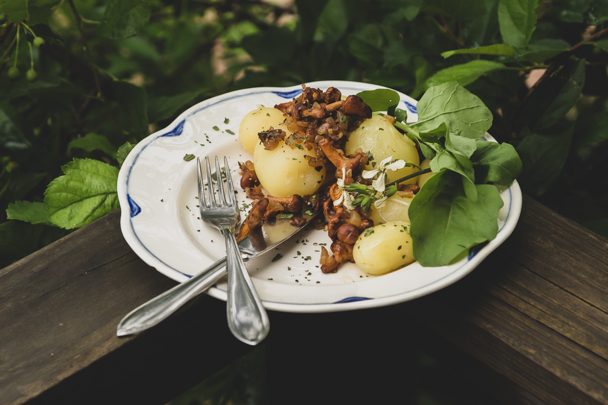 A plate of potatoes, chanterelles and onions with a side of wild arugula and flowers.